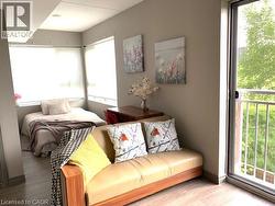 Compact living space featuring wood-finish flooring, light grey walls, and a large sliding glass door opening to a balcony with white railings - 