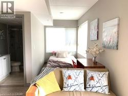 Light-filled living area featuring wood-finish flooring, a bright window with roller shades, and direct access to a full bathroom with a white vanity and a glass-enclosed shower - 