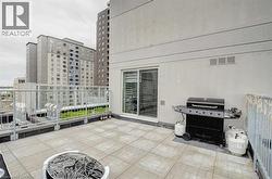 Spacious outdoor terrace with tiled flooring, featuring a sliding glass door entry, metal railing, and high-rise building backdrop - 