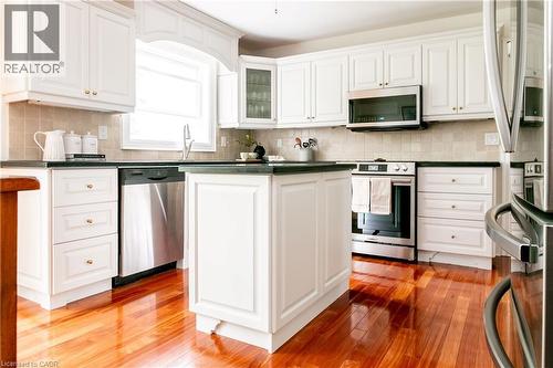 White cabinetry with gold-tone hardware, wood-finish flooring, stainless steel appliances, a center island, and a tiled backsplash - 1577 Old Spar Court, Mississauga, ON - Indoor Photo Showing Kitchen With Stainless Steel Kitchen With Upgraded Kitchen