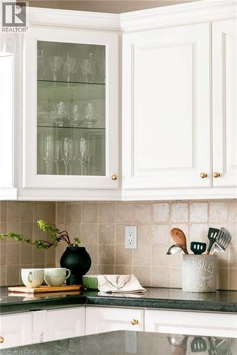 White upper cabinetry with gold-finish hardware, glass-front display cabinet, dark stone countertops, and a light-toned square tile backsplash - 1577 Old Spar Court, Mississauga, ON - Indoor Photo Showing Kitchen