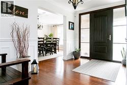 Inviting entryway featuring rich wood-finish flooring, a dark wood panel door with textured glass sidelights, and white wainscoting - 