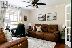 Bright interior room featuring a multi-pane window, crown molding, a ceiling fan with integrated lighting, and wood-finish flooring - 