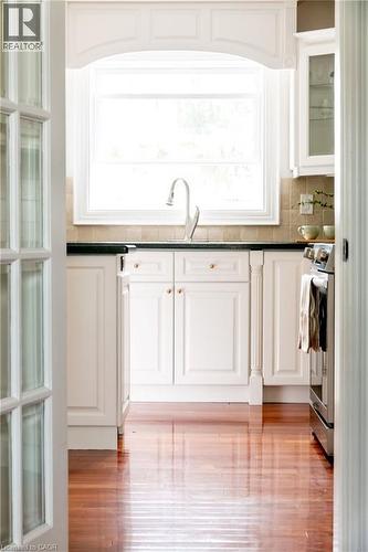 Kitchen area featuring wood-finish flooring, white cabinetry with gold-tone hardware, a large window with architrave detailing, a stainless steel faucet, and dark countertops - 1577 Old Spar Court, Mississauga, ON - Indoor Photo Showing Kitchen