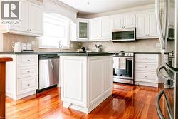 White cabinetry with gold-tone hardware, wood-finish flooring, stainless steel appliances, a center island, and a tiled backsplash - 