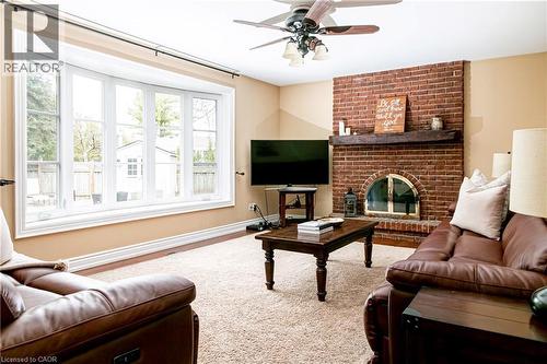 Living area featuring a brick fireplace with a wood-beam mantel, a large bay window, a ceiling fan, and carpet flooring - 1577 Old Spar Court, Mississauga, ON - Indoor Photo Showing Living Room With Fireplace