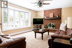 Living area featuring a brick fireplace with a wood-beam mantel, a large bay window, a ceiling fan, and carpet flooring - 