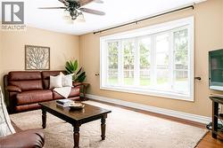 Living area featuring a prominent bay window with white trim, wood-finish flooring, and a ceiling fan with integrated lighting - 