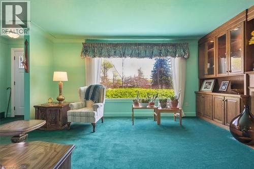 Spacious room featuring a prominent picture window, built-in wooden cabinetry with glass-front display cases, teal carpeting, and a contrasting light green wall color - 2117 Edinburgh Drive, Burlington, ON - Indoor