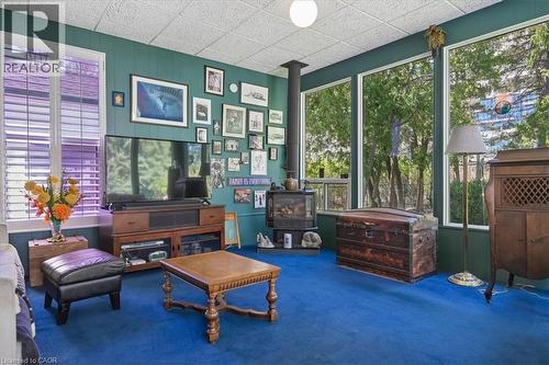 Spacious living area featuring a prominent wood-burning stove with a black stovepipe, a blue carpet, and paneling on the walls - 2117 Edinburgh Drive, Burlington, ON - Indoor
