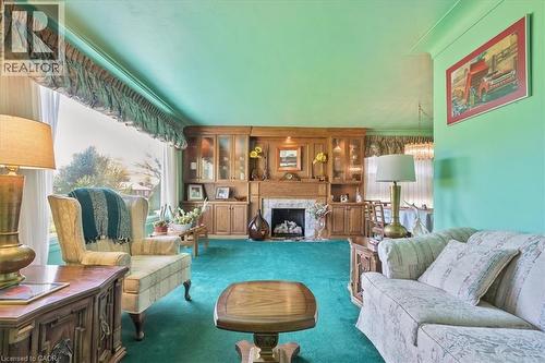 Living area featuring a stone-surround fireplace with a wood mantel, built-in wooden cabinetry with glass-front display sections, and a large picture window - 2117 Edinburgh Drive, Burlington, ON - Indoor Photo Showing Living Room With Fireplace