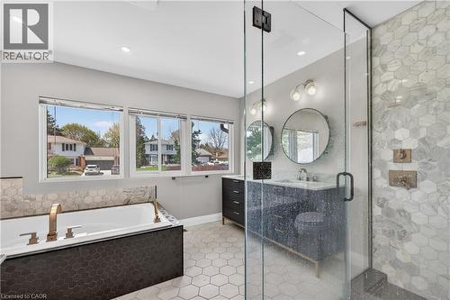 Contemporary bathroom featuring a frameless glass shower enclosure, a built-in soaking tub with dark hexagon tile surround, and a double vanity with round mirrors - 515 Bobbybrook Drive, London, ON - Indoor Photo Showing Bathroom