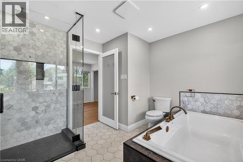 Bathroom featuring a frameless glass shower enclosure with hexagonal tile, a built-in soaking tub with bronze fixtures, hexagonal floor tiling, and recessed lighting - 515 Bobbybrook Drive, London, ON - Indoor Photo Showing Bathroom