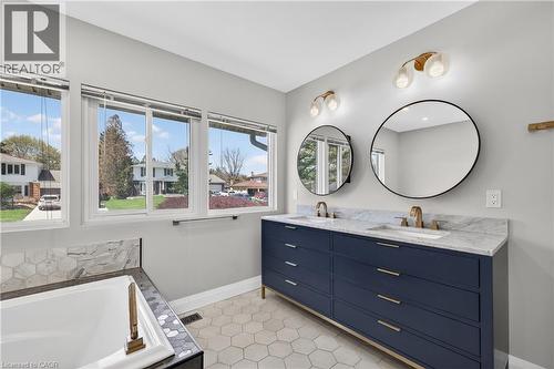 Bathroom featuring a double vanity with a blue cabinet and brass hardware, round mirrors, and dual wall-mounted light fixtures - 515 Bobbybrook Drive, London, ON - Indoor Photo Showing Bathroom