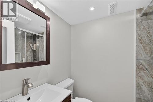 Bathroom featuring a framed mirror, vanity with an integrated sink and brushed nickel faucet, white toilet, and a tiled shower enclosure with a glass door - 515 Bobbybrook Drive, London, ON - Indoor Photo Showing Bathroom