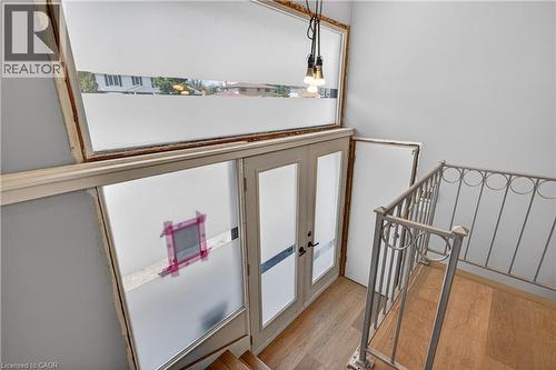 Stairwell featuring light wood-finish flooring, a decorative metal railing, a built-in pendant light fixture, and double glass-paneled doors with frosted lower sections - 515 Bobbybrook Drive, London, ON - Indoor Photo Showing Other Room