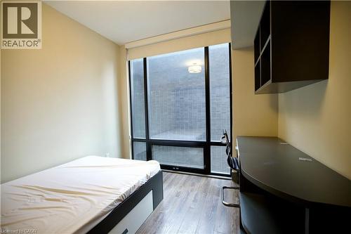 Room featuring full-height window with roller shade, wood-finish flooring, built-in desk, and wall-mounted shelving - 330 Phillip Street Unit# S605, Waterloo, ON - Indoor Photo Showing Bedroom