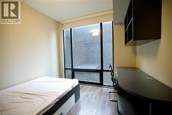 Room featuring full-height window with roller shade, wood-finish flooring, built-in desk, and wall-mounted shelving - 