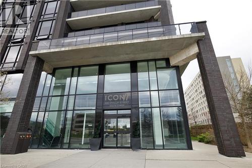 Building entrance featuring a glass facade with black framing, concrete overhang, and brick-clad supports - 330 Phillip Street Unit# S605, Waterloo, ON - Outdoor