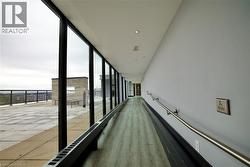 Rooftop access corridor featuring full-height windows, wood-finish flooring, recessed ceiling lights, and a continuous handrail - 