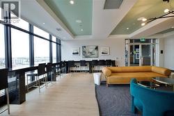 Expansive communal lounge area featuring a full wall of floor-to-ceiling windows, light wood-finish flooring, and a recessed ceiling design with integrated lighting - 