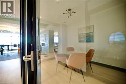 Glass-enclosed room featuring wood-finish flooring, a contemporary chandelier, and a wall-mounted art piece - 