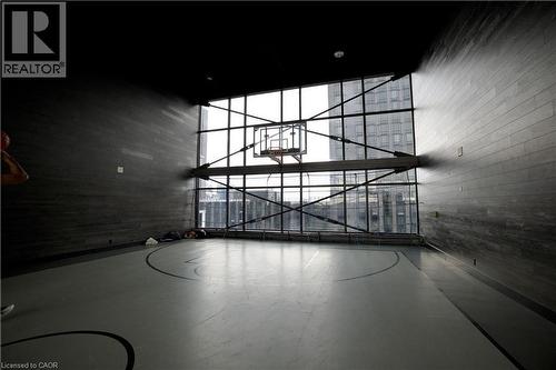 Indoor basketball court featuring a full-height glass wall, high ceilings, dark wood-finish wall paneling, a full basketball hoop, and painted court lines on the flooring - 330 Phillip Street Unit# S605, Waterloo, ON - Indoor Photo Showing Other Room
