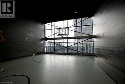 Indoor basketball court featuring a full-height glass wall, high ceilings, dark wood-finish wall paneling, a full basketball hoop, and painted court lines on the flooring - 