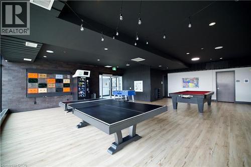 Open-concept recreation area featuring light wood-finish flooring, a dark ceiling with recessed lighting, and a brick-pattern accent wall - 330 Phillip Street Unit# S605, Waterloo, ON - Indoor Photo Showing Garage