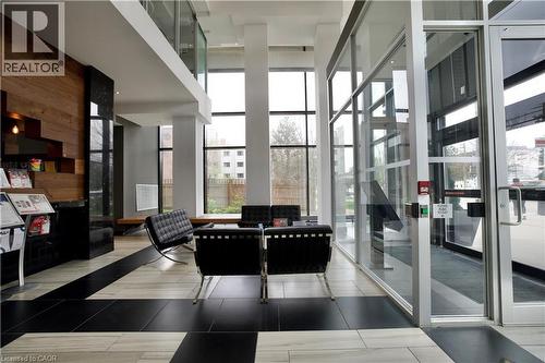 Double-height lobby featuring a wood-panel accent wall, black and light-toned tile flooring, floor-to-ceiling windows, and an upper-level glass railing - 330 Phillip Street Unit# S605, Waterloo, ON - Indoor Photo Showing Other Room