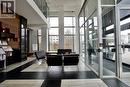 Double-height lobby featuring a wood-panel accent wall, black and light-toned tile flooring, floor-to-ceiling windows, and an upper-level glass railing - 330 Phillip Street Unit# S605, Waterloo, ON  - Indoor Photo Showing Other Room 