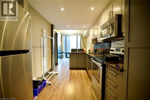 Modern kitchen featuring wood-finish flooring, recessed lighting, stainless steel appliances, dark countertops, and light-toned cabinetry with contemporary hardware - 330 Phillip Street Unit# S605, Waterloo, ON - Indoor Photo Showing Kitchen