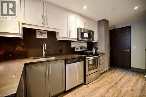 Compact kitchen featuring white upper cabinetry, gray lower cabinetry, and a dark brown backsplash - 330 Phillip Street Unit# S605, Waterloo, ON - Indoor Photo Showing Kitchen With Stainless Steel Kitchen