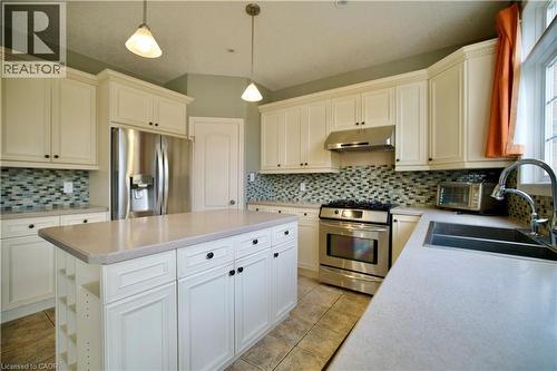 Kitchen featuring a central island with integrated storage, stainless steel appliances, white cabinetry with crown molding, a mosaic tile backsplash, and a double basin sink - 711 Cedar Bend Drive, Waterloo, ON - Indoor Photo Showing Kitchen With Stainless Steel Kitchen With Double Sink With Upgraded Kitchen