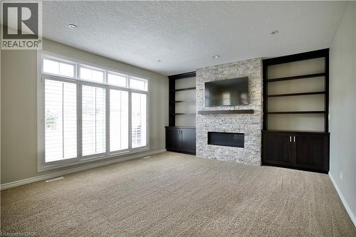Spacious room featuring a stone-clad fireplace with a recessed firebox, flanking built-in shelving with lower cabinetry, and a large window with white plantation shutters - 711 Cedar Bend Drive, Waterloo, ON - Indoor With Fireplace