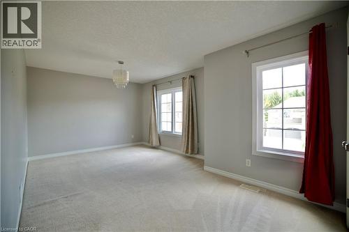 Neutral-toned room featuring light beige carpeting, multiple windows with white trim, a decorative ceiling light fixture, and light gray walls - 711 Cedar Bend Drive, Waterloo, ON - Indoor Photo Showing Other Room