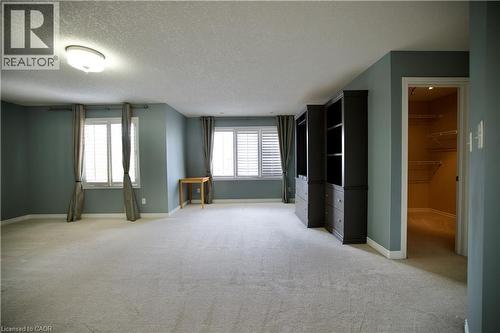 Spacious room featuring light gray carpeting, two windows with plantation shutters and drapes, two built-in dark wood storage units with shelving and drawers, and an open doorway to a walk-in closet w - 711 Cedar Bend Drive, Waterloo, ON - Indoor