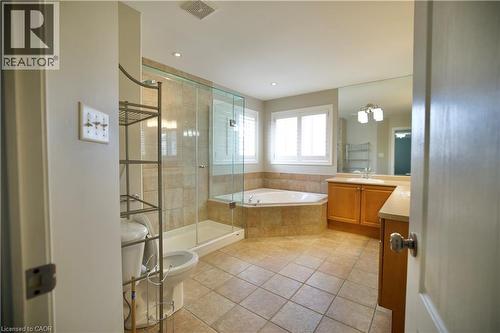 Spacious bathroom featuring tiled flooring, a corner soaking tub with tiled surround, a glass-enclosed shower, a vanity with ample countertop space, and dual windows with plantation shutters - 711 Cedar Bend Drive, Waterloo, ON - Indoor Photo Showing Bathroom