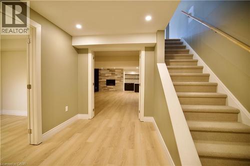 Carpeted staircase with white risers and railing, leading to a lower level featuring wood-finish flooring, recessed lighting, and a stone-clad fireplace with an electric insert - 711 Cedar Bend Drive, Waterloo, ON - Indoor Photo Showing Other Room