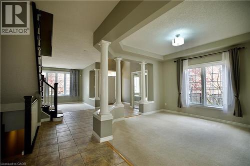 Open concept entryway featuring ceramic tile flooring, a carpeted living area, a classic white spindle staircase with dark wood-finish handrails, decorative fluted columns, and multiple windows with w - 711 Cedar Bend Drive, Waterloo, ON - Indoor Photo Showing Other Room