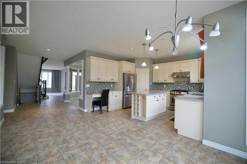 Spacious kitchen featuring cream cabinetry, a central island with integrated wine storage, stainless steel appliances, and a mosaic tile backsplash - 711 Cedar Bend Drive, Waterloo, ON - Indoor Photo Showing Kitchen