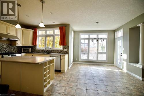 Kitchen and dining area featuring tile flooring, cream cabinetry, a center island with integrated shelving, and a large window with white plantation shutters - 711 Cedar Bend Drive, Waterloo, ON - Indoor Photo Showing Kitchen