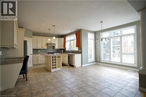 Spacious kitchen and dining area featuring ceramic tile flooring, cream cabinetry, a central island with wine storage, stainless steel appliances, and large windows with plantation shutters - 711 Cedar Bend Drive, Waterloo, ON - Indoor Photo Showing Kitchen With Upgraded Kitchen
