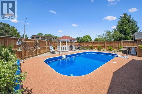 Private backyard featuring an in-ground swimming pool with surrounding textured decking, wooden privacy fencing, a white gazebo with a red roof, and mature plantings - 574 Sprucehill Avenue, Waterloo, ON - Outdoor With In Ground Pool With Backyard