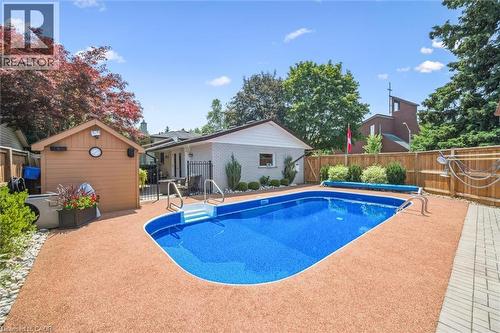 Backyard featuring a kidney-shaped swimming pool with steps, a surrounding aggregate patio, and a wood storage shed - 574 Sprucehill Avenue, Waterloo, ON - Outdoor With In Ground Pool With Backyard