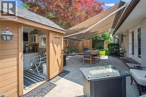 Outdoor paved patio featuring a built-in fire pit, retractable awning, and direct access to a functional shed with cabinetry and counter space - 574 Sprucehill Avenue, Waterloo, ON - Outdoor With Deck Patio Veranda With Exterior