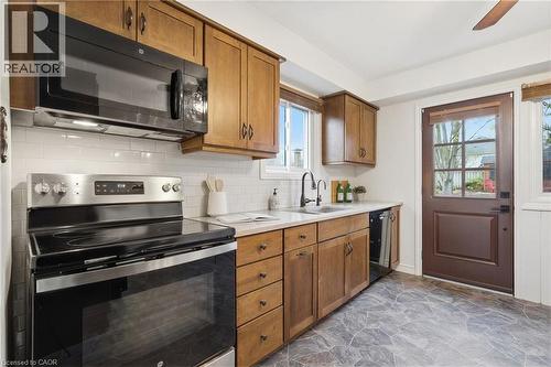 Kitchen featuring wood-finish cabinetry, tile backsplash, stainless steel appliances, a deep basin sink with a black faucet, and a paneled glass-insert door - 56 Angela Crescent, Cambridge, ON - Indoor Photo Showing Kitchen With Double Sink
