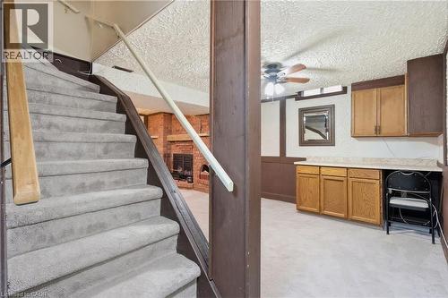 Carpeted staircase descending to a lower level featuring a prominent brick fireplace - 56 Angela Crescent, Cambridge, ON - Indoor Photo Showing Other Room