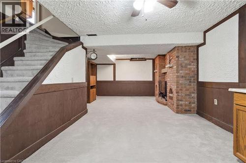 Spacious recreation room featuring a brick gas fireplace, wood paneling, carpeted flooring, and a ceiling fan - 56 Angela Crescent, Cambridge, ON -  Photo Showing Other Room