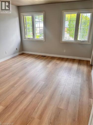 Spacious room featuring two large windows with white trim, light neutral wall paint, and wood-finish flooring - 206 Northmanor Crescent, Kitchener, ON 